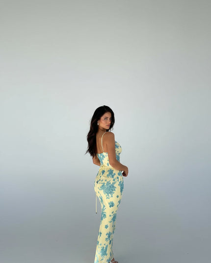 Back view of a women's yellow floral maxi dress showing the adjustable straps and subtle side ruching, with blue floral pattern.