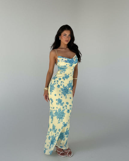 Full-length view of a women's yellow floral cowl neck maxi dress with blue flowers and adjustable straps, paired with white heels.