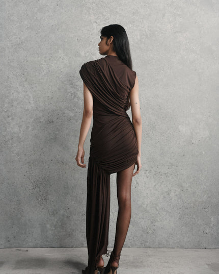Rear view of a woman wearing the brown ruched asymmetrical mini maxi dress with sheer black tights and high heels.