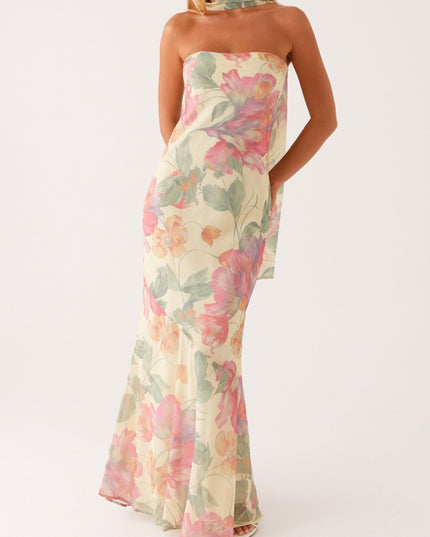 Women's strapless floral maxi dress in light yellow with pink and green flowers, featuring an asymmetrical hem and flowing scarf detail.