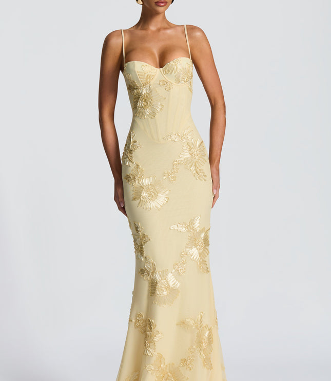 Front view of a woman standing in a light yellow floral corset maxi dress with gold embroidered details and a sweetheart neckline.