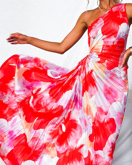 Close up of the flowing pleated skirt of a red and pink floral print one-shoulder maxi dress with cut-out.