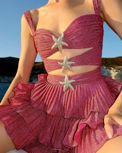 Women's shimmery coral summer mini dress with cut-outs and silver starfish details, worn outdoors.