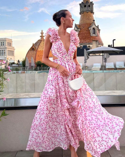 Women's pink floral print maxi dress with deep V-neck, ruffled sleeves, and side cut-outs, worn on a rooftop.