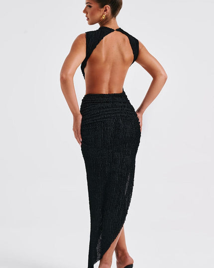 Full back view of a black sleeveless mock neck midi dress featuring a cut-out back and an asymmetrical hem, worn with black heels.