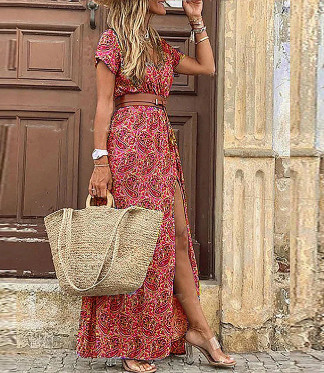 Women's red and pink paisley floral print short sleeve maxi dress with a brown belt and side slit, holding a straw bag.