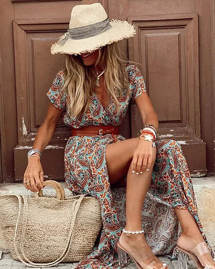 Women's rust and teal paisley floral print short sleeve maxi dress with a brown belt, seated, wearing a straw hat.