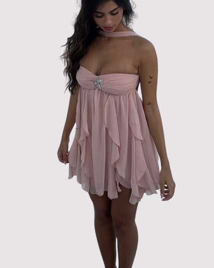 Woman in a light pink summer ruffle mini dress with a halter neck and layered ruffles, standing against a white background.