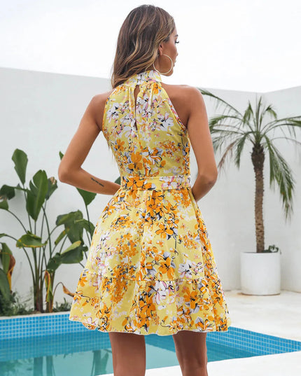 Back view of a yellow floral halter neck tiered mini dress, showing the keyhole and tied waist detail, with a palm tree in background.