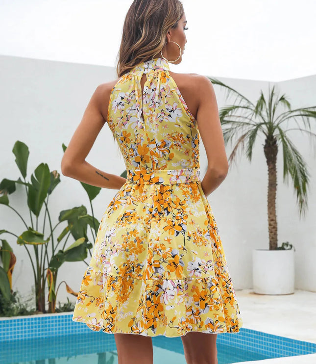 Back view of a yellow floral halter neck tiered mini dress, showing the keyhole and tied waist detail, with a palm tree in background.