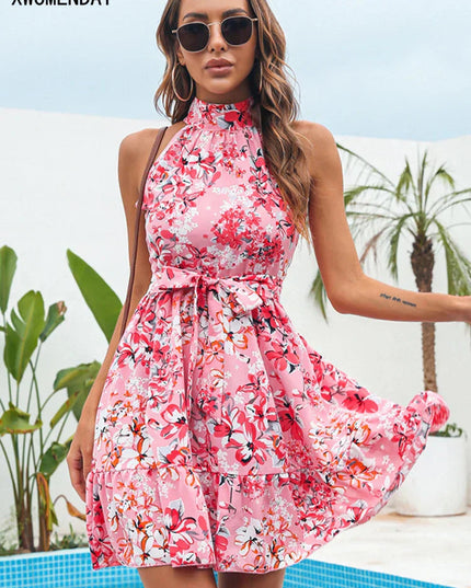 Pink floral halter neck tiered mini dress with a tie-waist, worn outdoors by a pool.