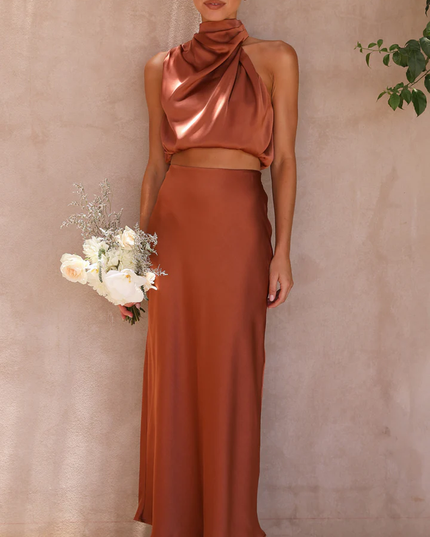 Front view of a women's rust orange satin high neck crop top and maxi skirt set, holding a white floral bouquet.