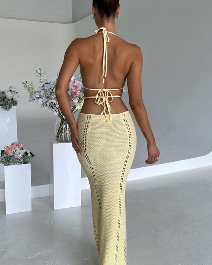 Back view of a women's light yellow crochet knit maxi dress, showing the halter tie closure and open back design.