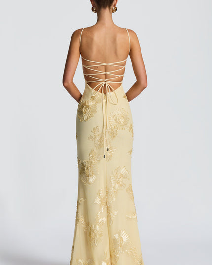 Back view of a woman in a light yellow floral lace-up maxi dress, showcasing the intricate lace-up detail and gold embroidery.