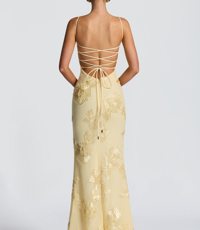 Back view of a woman in a light yellow floral lace-up maxi dress, showcasing the intricate lace-up detail and gold embroidery.