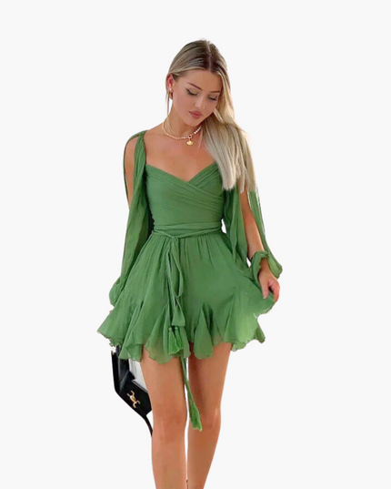 Blonde woman wearing a green V-neck mini dress with long open sleeves and a tie waist on a white background.