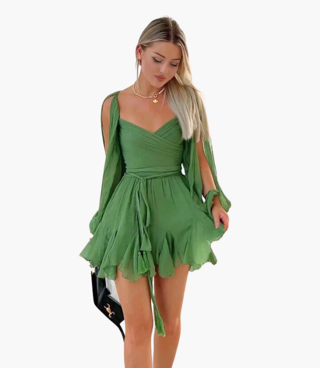 Blonde woman wearing a green V-neck mini dress with long open sleeves and a tie waist on a white background.