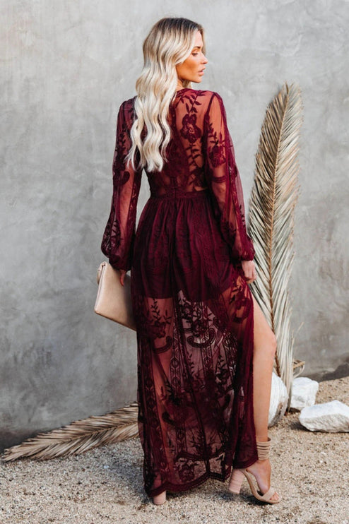 Back view of a women's deep burgundy lace long sleeve V-neck maxi dress, showcasing sheer skirt details.