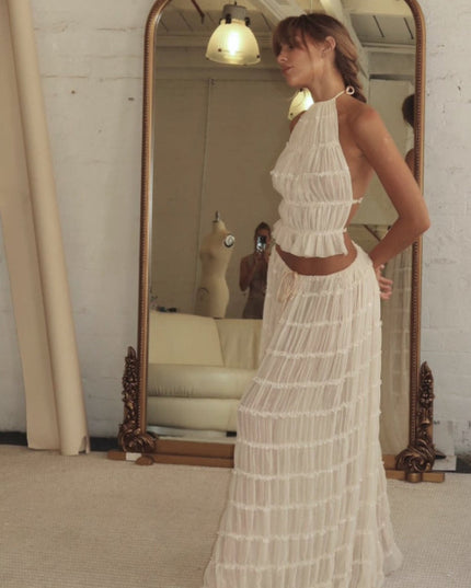 Side profile of a woman wearing the ivory halter ruffle trim crop top and maxi skirt set, reflected in a vintage mirror.