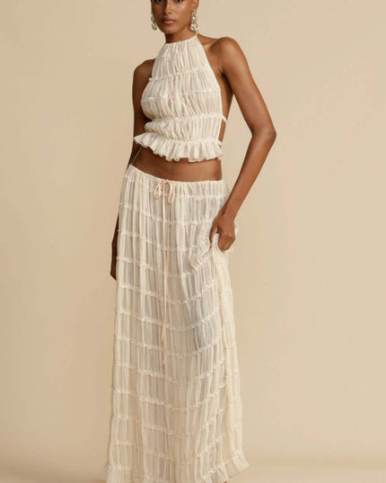 Full-length view of a women's ivory halter ruffle trim crop top and matching maxi skirt set, featuring delicate ruffles and a drawstring waist.