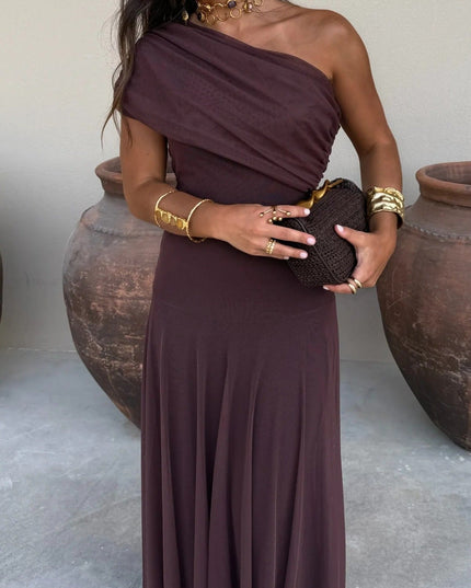 Women's chocolate brown drape one shoulder mesh maxi dress, styled with gold jewelry and a woven clutch.