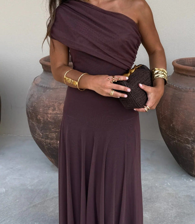 Women's chocolate brown drape one shoulder mesh maxi dress, styled with gold jewelry and a woven clutch.
