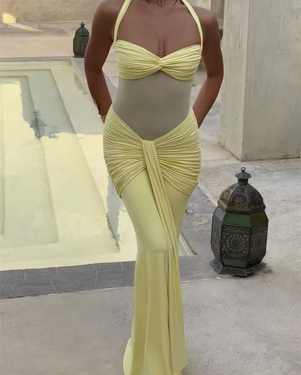 Front view of a women's pastel yellow prom dress, featuring a halter neckline, ruched details, and a flowing maxi skirt, in an outdoor setting.