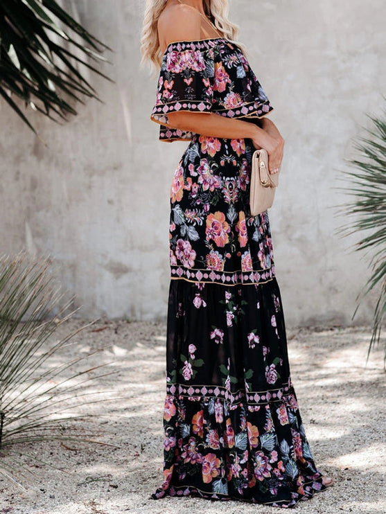 Side view of a women's black floral off-shoulder maxi dress, featuring a tiered skirt and vibrant pink and purple blossoms.