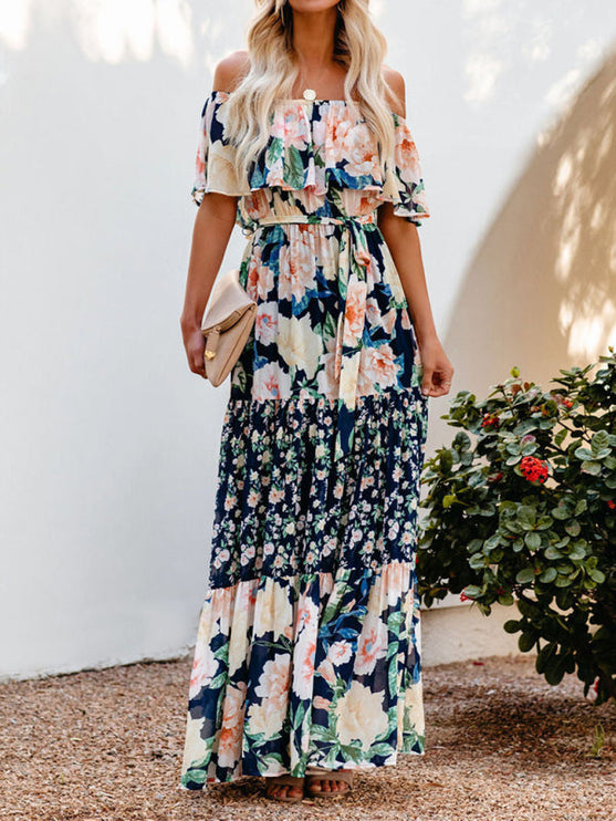 Women's off-shoulder ruffled floral maxi dress in navy blue with large peach and cream flowers, cinched waist, and tiered skirt.