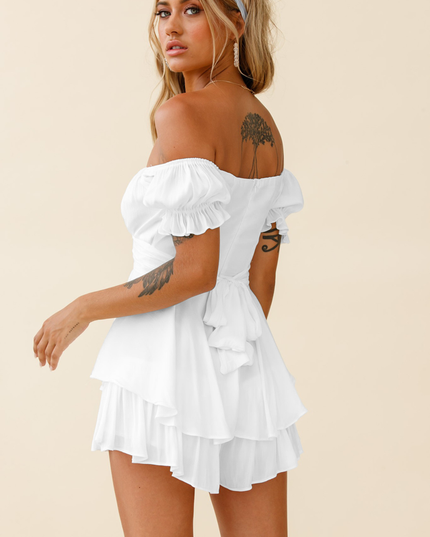 Back 3/4 view of a white off-shoulder summer romper, highlighting the tiered ruffles, tie-back detail, and short length.