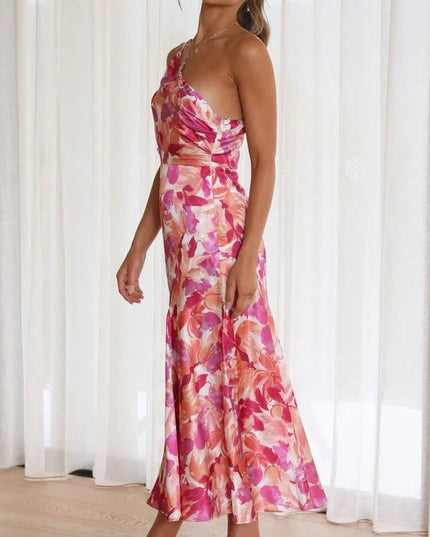Side profile of a woman wearing a pink and orange floral one-shoulder ruched bust midi dress, with a flowing skirt.