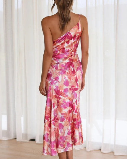 Back view of a woman in a vibrant pink and orange floral one-shoulder midi dress, showcasing the draped back.