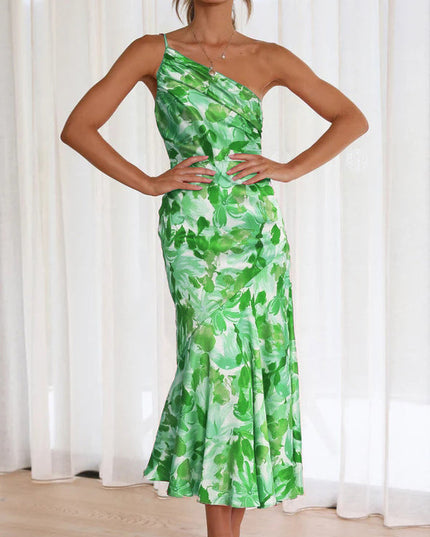 Front view of a woman wearing a green and white floral one-shoulder ruched bust midi dress, with hands on hips.
