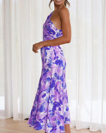 Side profile of a woman in a purple and white floral one-shoulder midi dress, highlighting the dress's cut and print.