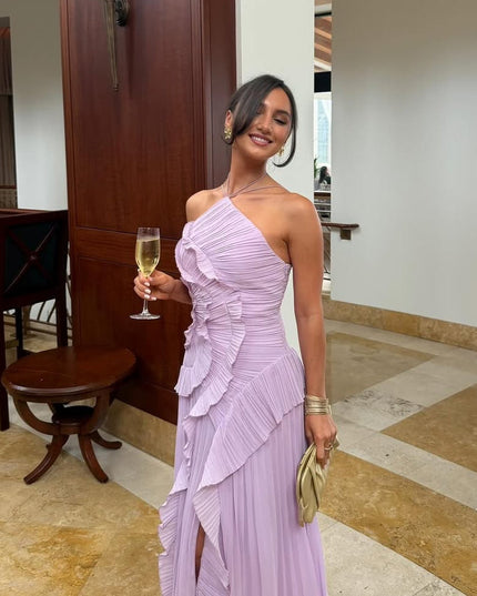 Women's lavender one-shoulder dress with a ruffled bodice and pleated skirt, styled with a champagne flute and gold clutch.