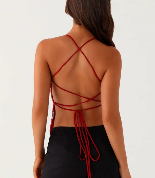 Back view of a red sequin V-neck cami top showing criss-cross strap detailing and tie closure, worn with black shorts.