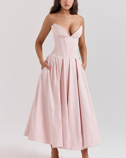 Side view of a pink strapless boned bodice midi dress, showing the pleated skirt and pockets, with white heels.