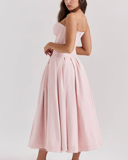 Side profile of a woman in a light pink strapless boned bodice pleated midi dress with white kitten heels.
