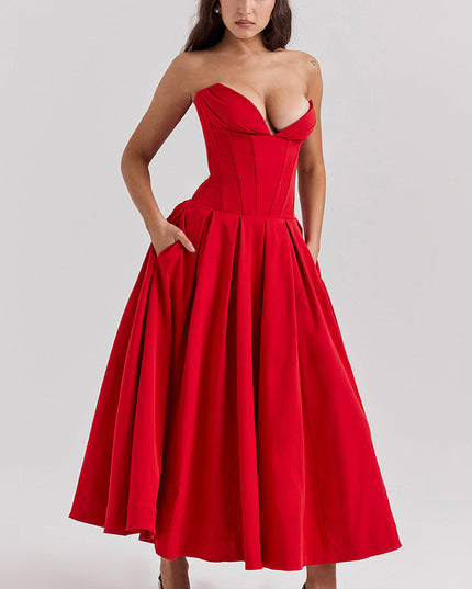 Woman with hands in pockets of a red strapless boned bodice pleated midi dress, highlighting the practical design.