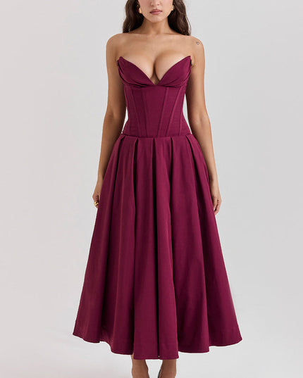 Front view of a woman in a deep burgundy strapless boned bodice pleated midi dress with matching heels.