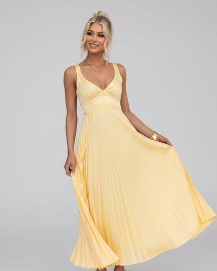 Women's yellow V-neck pleated maxi dress with cut-out details, flowing skirt, and gold heels.