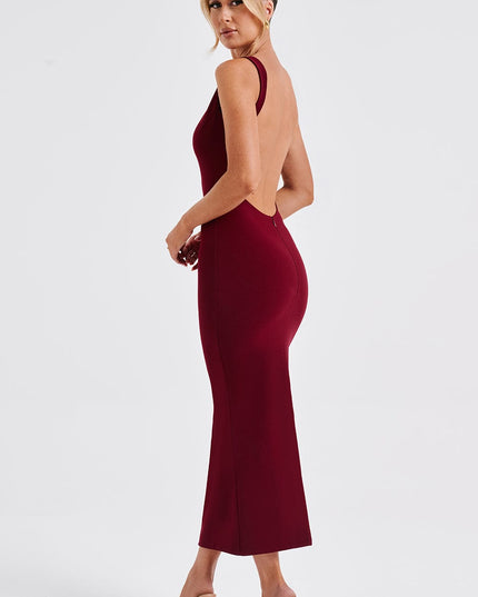 Side profile of a women's burgundy midi dress, emphasizing the low back and tailored fit, paired with nude heels.