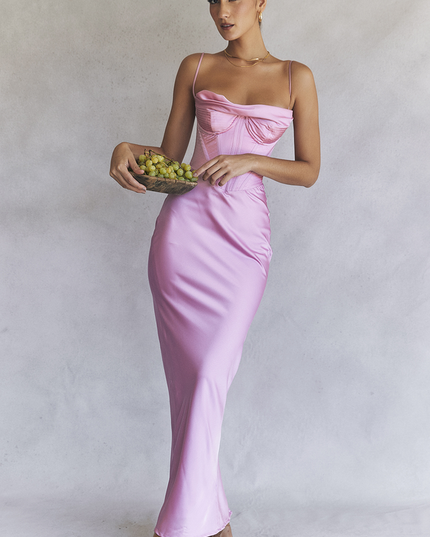 Women's pink satin corset plunge neck maxi dress, featuring a draped neckline and structured bodice, holding a bowl of grapes.