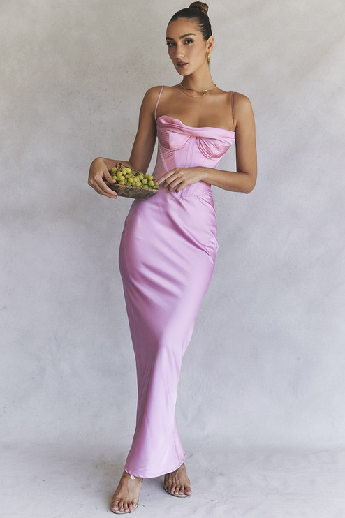 Women's pink satin corset plunge neck maxi dress, featuring a draped neckline and structured bodice, holding a bowl of grapes.