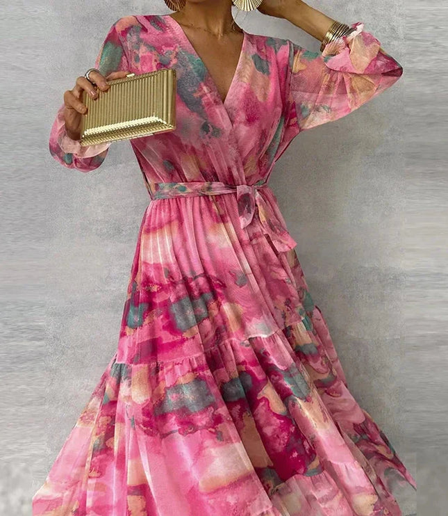 Full-length view of a women's pink floral long sleeve maxi dress with a V-neck and ruffled cuffs, holding a clutch.
