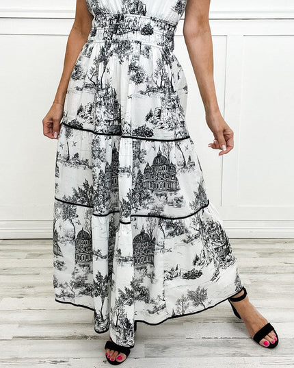 White and black toile print maxi dress with tiered skirt and smocked waist, featuring a detailed scenic pattern.