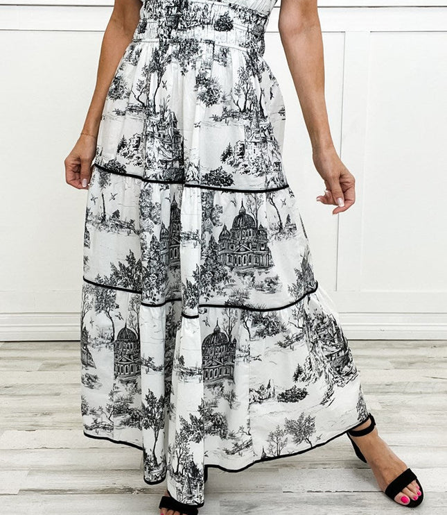 White and black toile print maxi dress with tiered skirt and smocked waist, featuring a detailed scenic pattern.