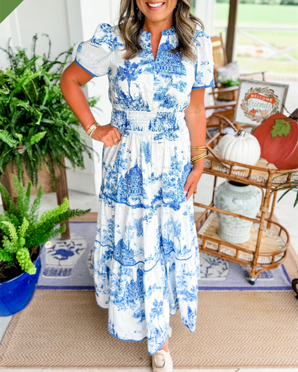 Women's white summer maxi dress featuring blue scenic print, v-neck, short sleeves, tiered skirt, and smocked waist, with white slides.