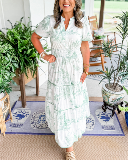 Women's white summer maxi dress with light green scenic print, v-neck, short sleeves, and smocked waist, with woven slides.
