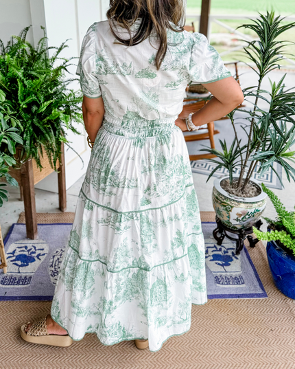 Back view of women's white summer maxi dress with light green scenic print, short sleeves, and smocked waist, with platform slides.